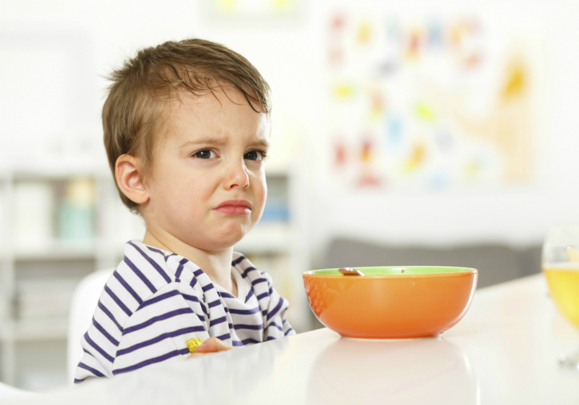 Unhappy young child eating breakfast 